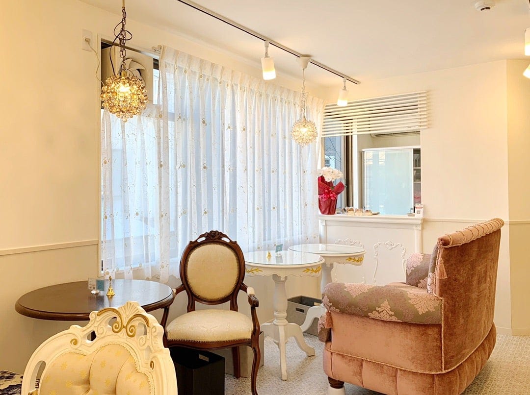 Phto of the interior of a cafe styled with luxurious velvel and damask furniture and oranate white and mahogany tables. 