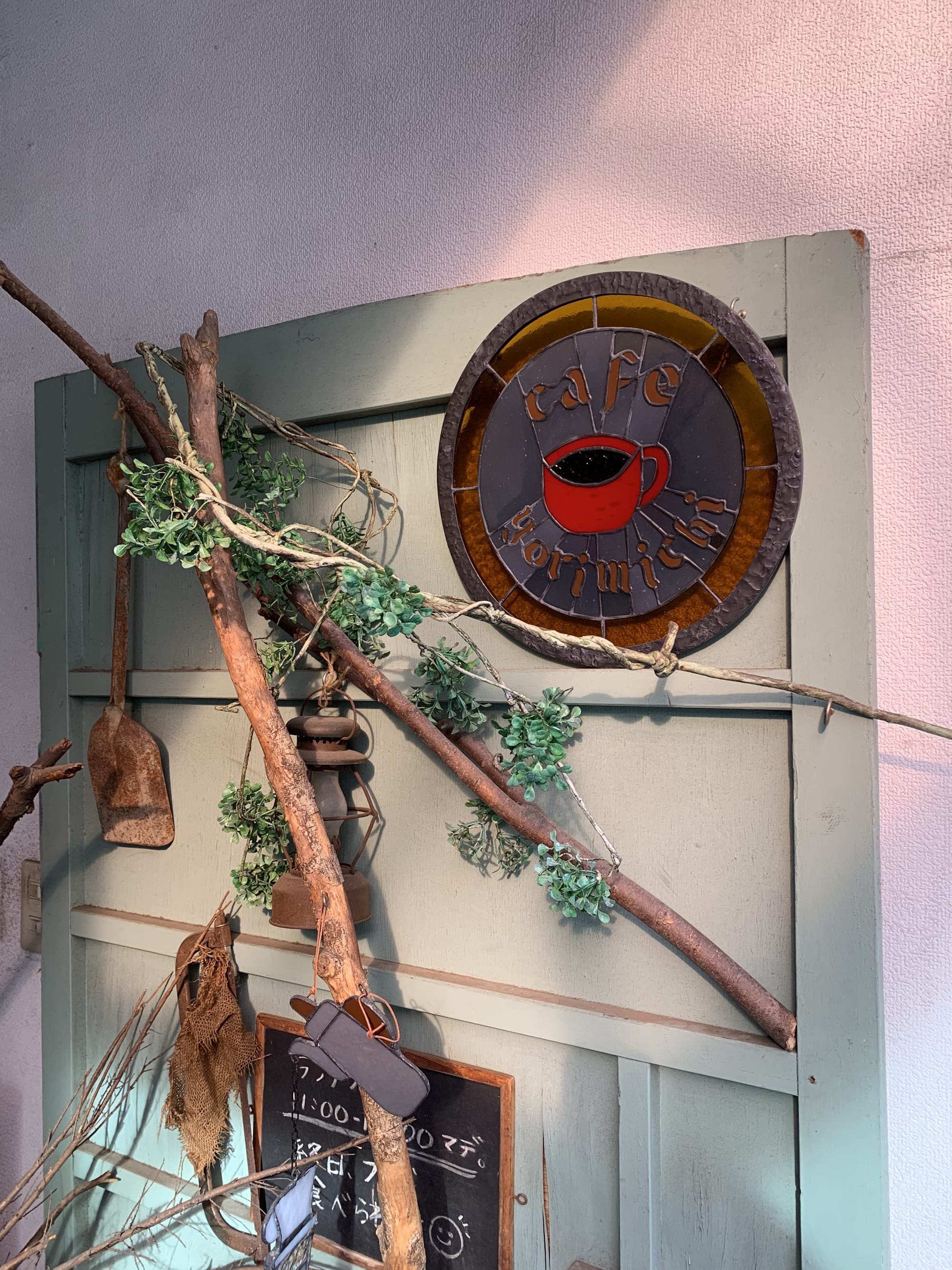 Photo a of a cafe door with banches and burlap decoration. Overhead a stained glass circular sign says Cafe Yorimichi