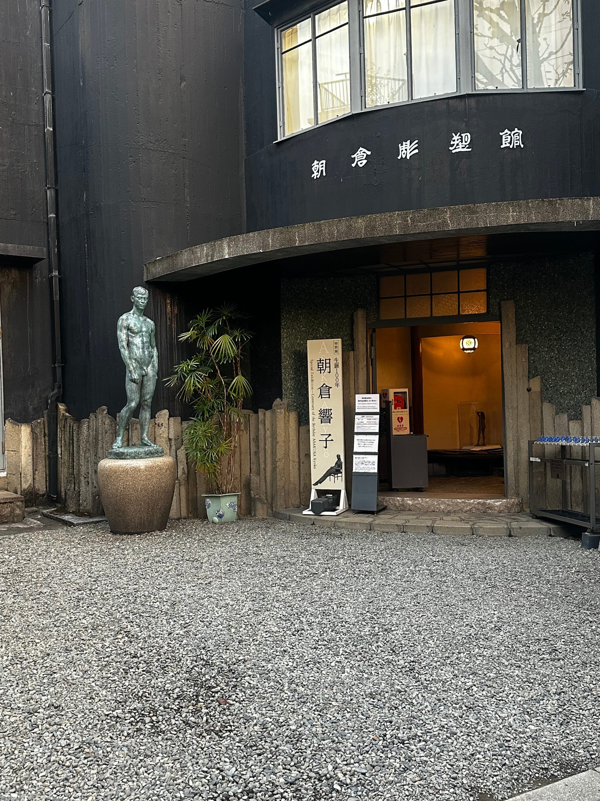 A photo a black building that is curved in shape. The entryway isopen and nect to it there is a sculpture of a nude man.