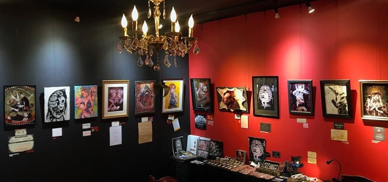 photo of a black ared room with various horror themedart on the walls. In the middle of the room a golden chandelier hangs from the ceiling