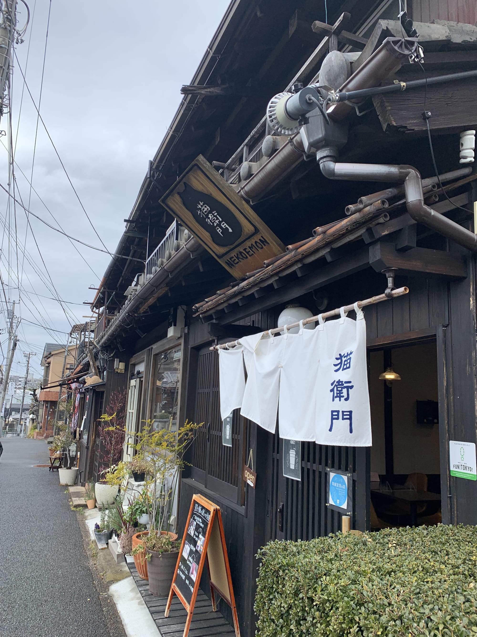 Phto of a tradiotina japanese house. The sign board has the shape of of a cat on it and reads neko e mon in Japanese characters 