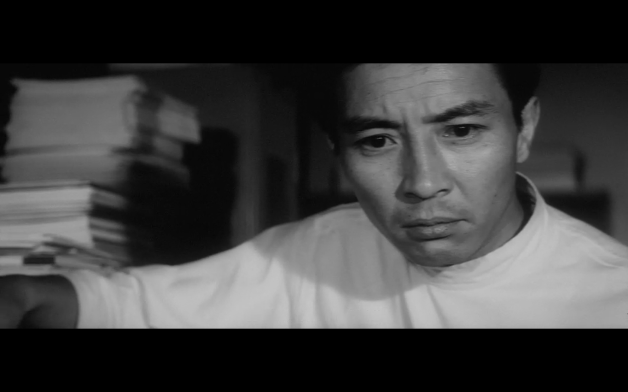 A man wearing a doctor's coat rests his arm on something. He has an uncertain expression on his face.
