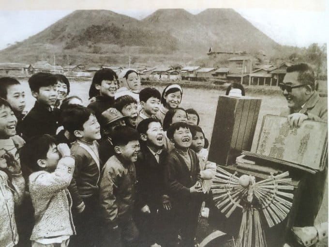 A street performing showing Graveyard Kitaro to a crowd of children.